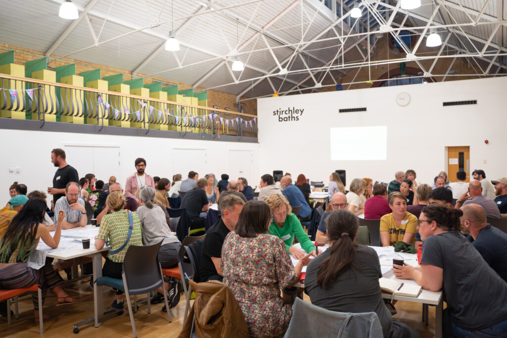 Image shows around one hundred people say around tables in Stirchley Baths centre for the first Stirchley Community Plan meeting